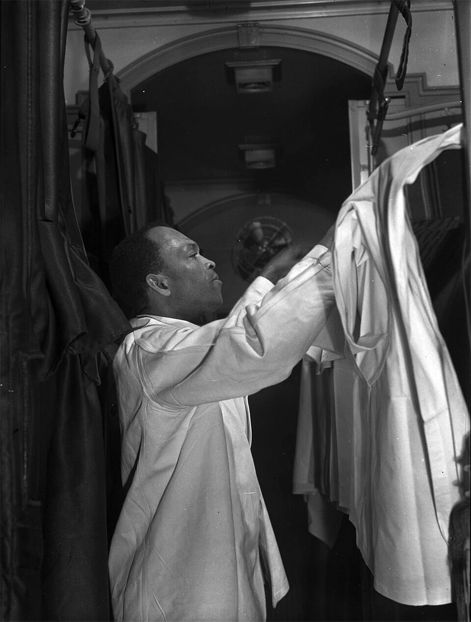A photograph of a Pullman porter in uniform reaching up to make up an upper berth in a sleeping car.